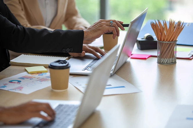 Team members’ hands pointing at a laptop screen during a meeting, symbolizing collaboration, discussion, and shared decision-making in a professional setting.